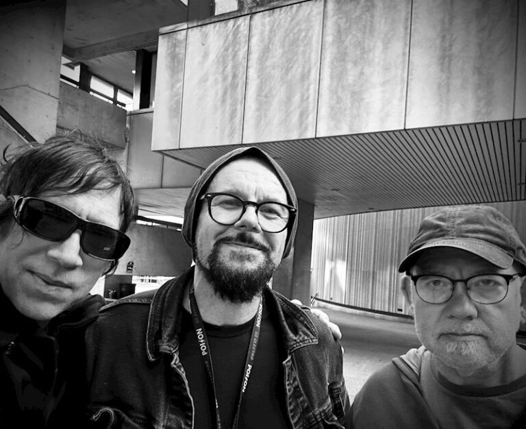 Black and white Lowsunday press photo of three men in front of a brutalist concrete building