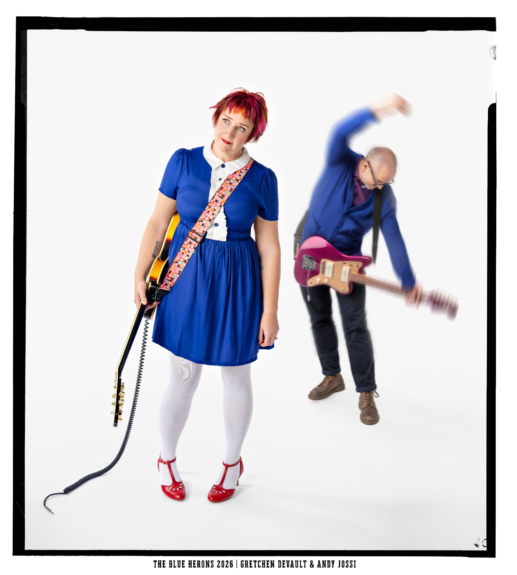 The Blue Herons: Gretchen DeVault in a blue dress and red shoes holding a sunburst guitar, with Andy Jossi blurred behind her swinging a pink Jazzmaster-style guitar