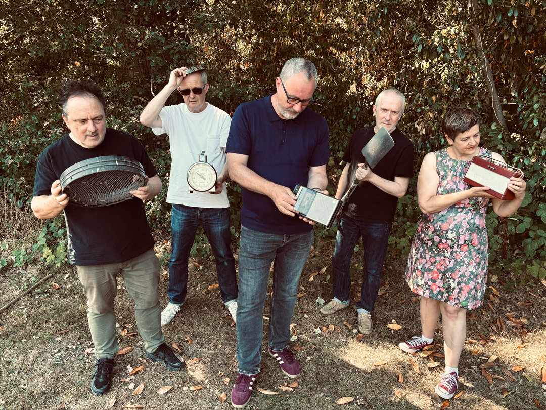 Swansea Sound - five band members standing in front of a hedge, each holding an old object: a garden sieve, a weighing scale, a transistor radio, a spade and a red portable radio